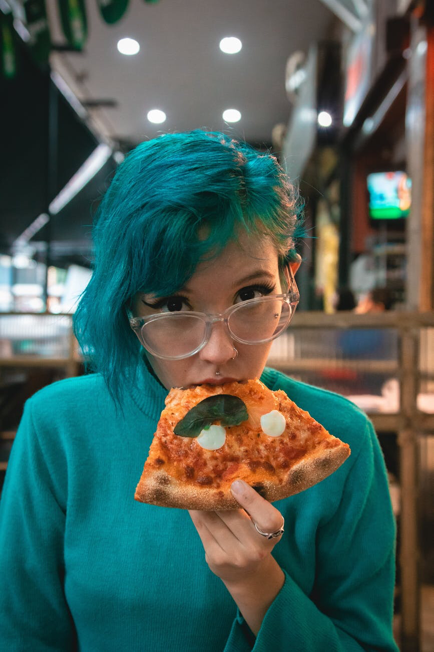 Woman with blue hair eating pizza